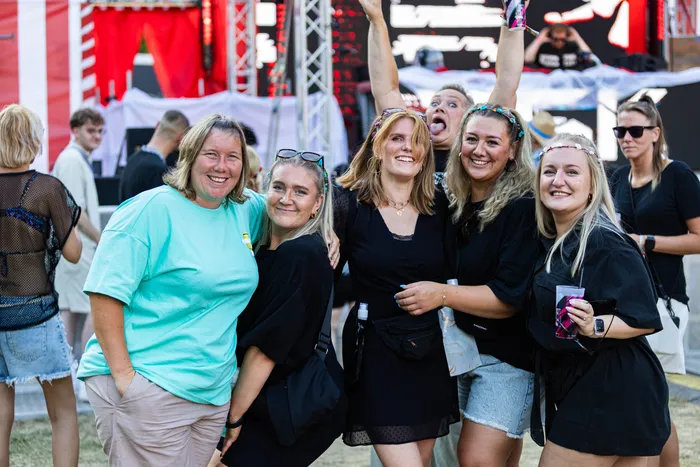 Eine Gruppe lächelnder junger Menschen posiert bei einem Festival im Freien.