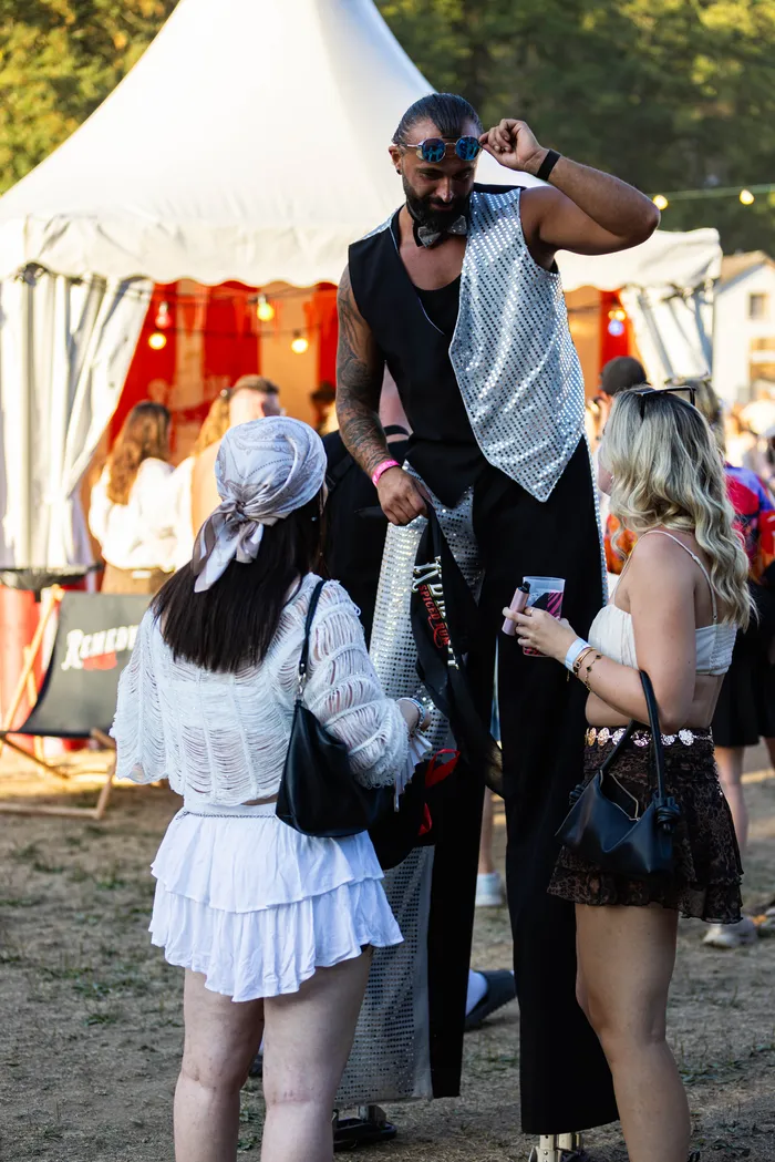 Ein Mann in silberner Paillettenweste und Fliege unterhält sich mit zwei Frauen vor einem weißen Festzelt beim Ferik Festival.
