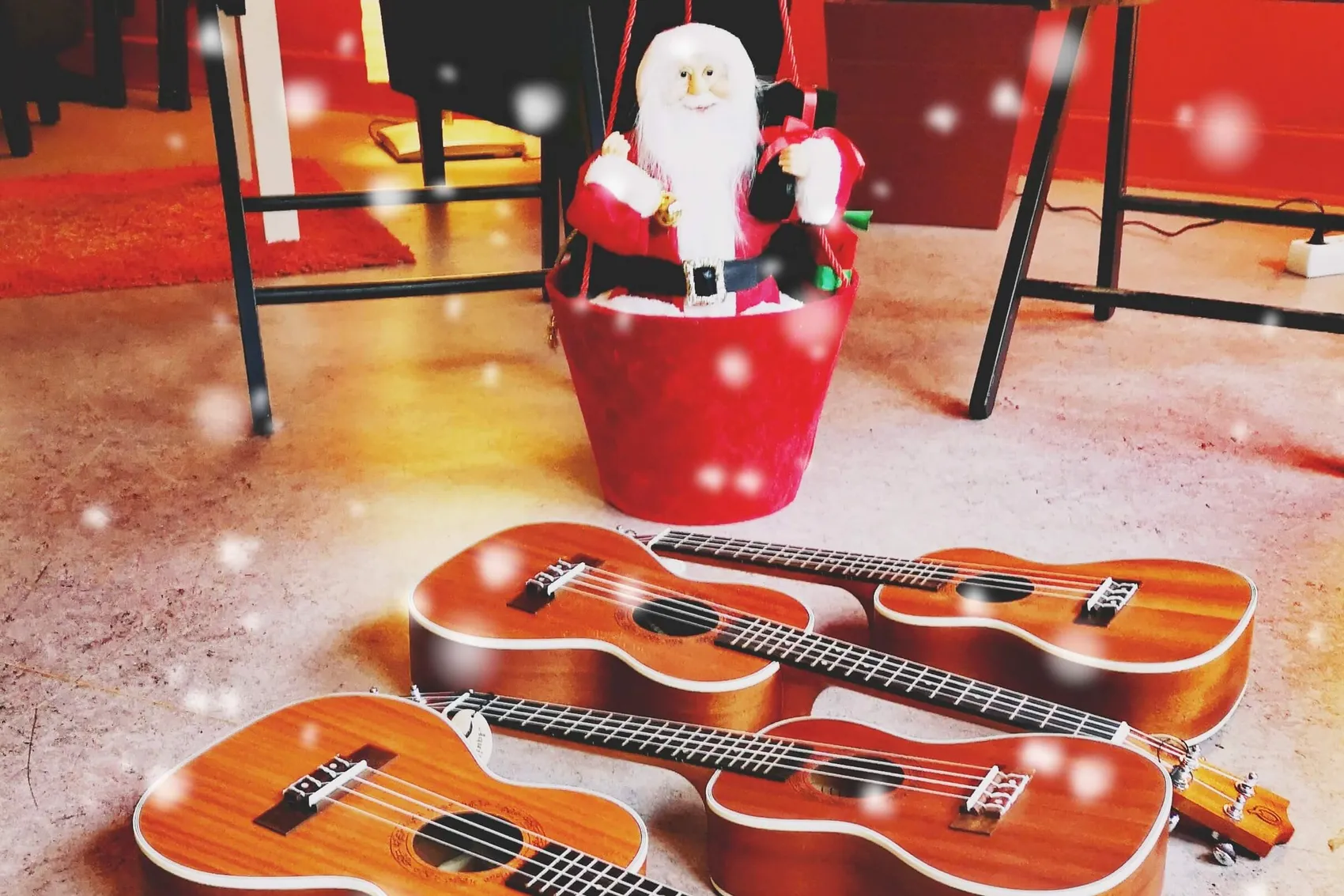 Drei Ukulelen liegen auf dem Boden vor einer Weihnachtsmann-Figur in einem roten Eimer.