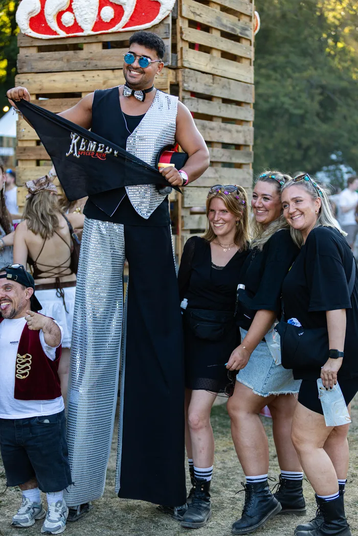 Ein Mann auf Stelzen in einem glitzernden silber-schwarzen Outfit hält eine schwarze Fahne mit der Aufschrift „KEMET“ auf dem Ferik Festival.