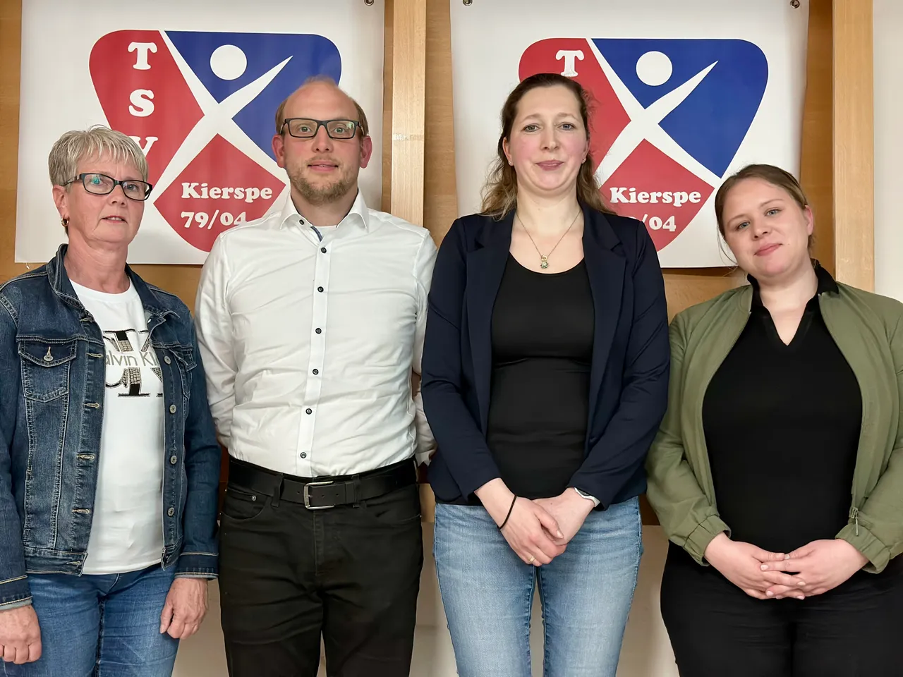 Vier Personen stehen nebeneinander vor einem Hintergrund mit dem Logo des TSV Kierspe. Von links: eine Frau mit kurzem, grauem Haar, ein Mann mit Brille, eine Frau mit langen, blonden Haaren und eine junge Frau mit langen, dunklen Haaren.