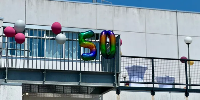 Farbige Folienballons in Form der Zahl 50 sind vor dem Gebäude der Bibliothek in Kierspe angebracht. Im Hintergrund sind weitere Ballons und Tische zu sehen.