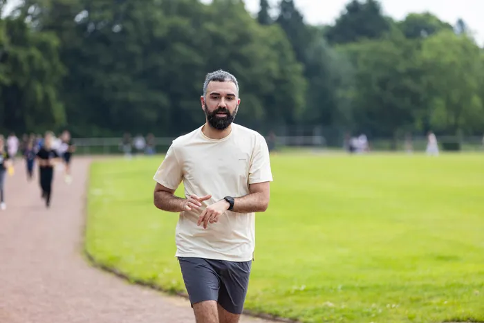 Ein Mann mit Bart und kurzrasiertem Haar läuft auf einem Weg in einem Park. Im Hintergrund sind weitere Läufer und eine grüne Wiese zu sehen.