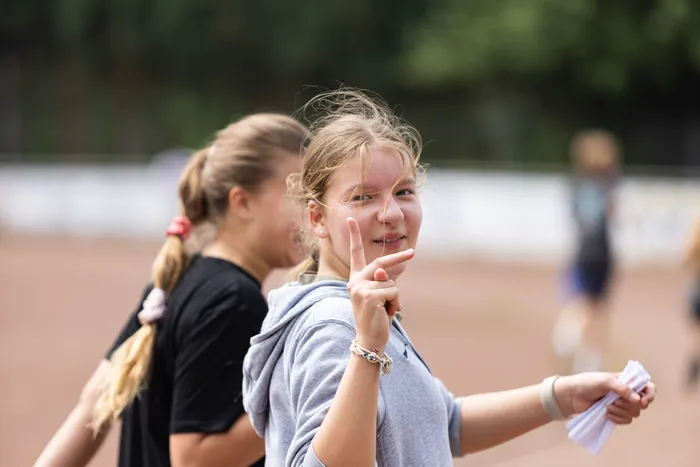 Ein Mädchen zeigt beim Sponsorenlauf der Gesamtschule Kierspe das Victory-Zeichen. Im Hintergrund sind weitere Schülerinnen und Schüler auf einer Laufbahn zu sehen.