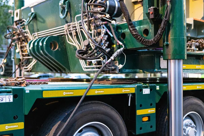 Nahaufnahme der hydraulischen Leitungen und der grünen Metallstruktur eines Schwertransport-Fahrzeugs.