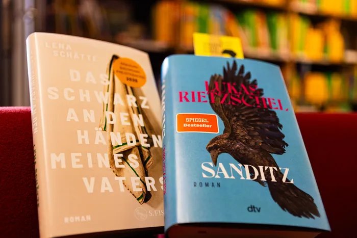 Zwei Bücher stehen nebeneinander: „Das Schwarz an den Händen meines Vaters“ von Lena Schätte und das hellblaue Buch „Sanditz“ von Lukas Rietzschel.
