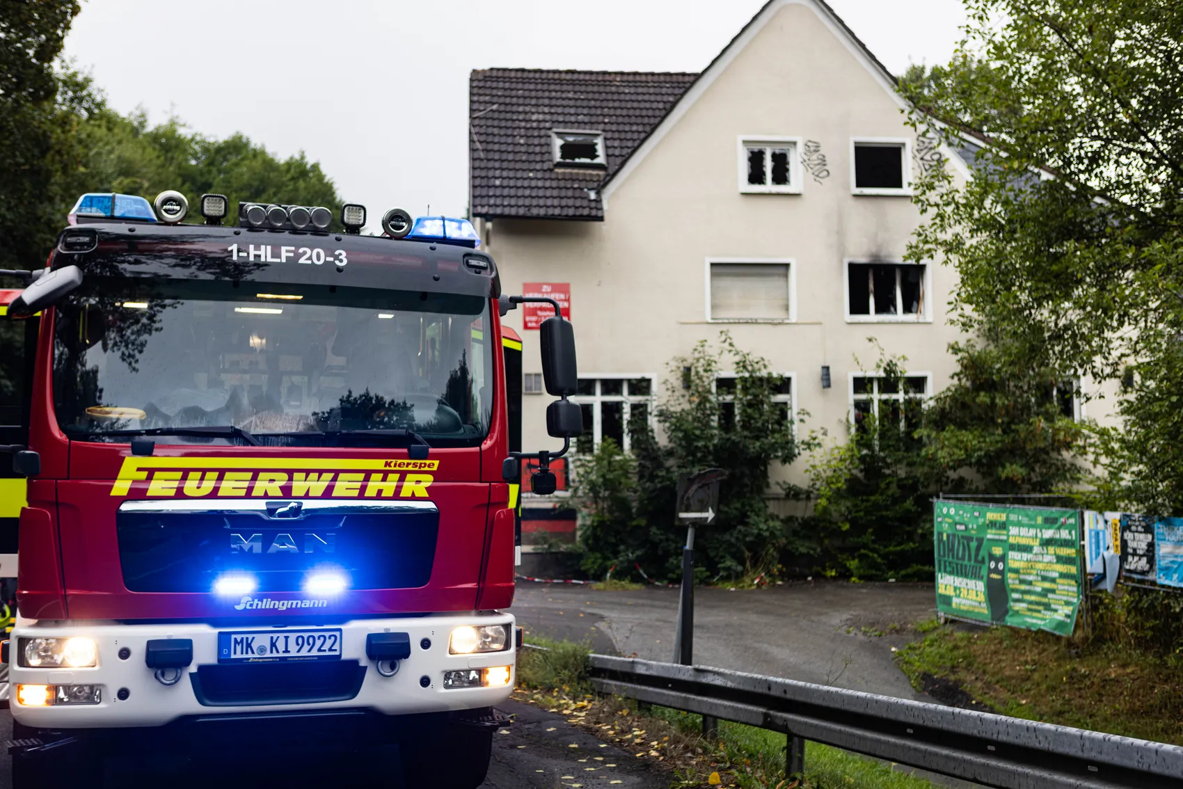 Ein rotes Feuerwehrfahrzeug der Feuerwehr Kierspe vor einem weißen Gebäude mit Brandspuren an den Fenstern.