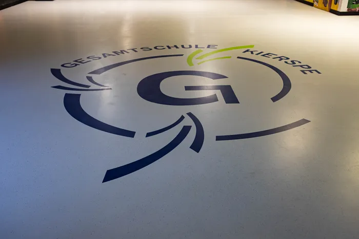 Logo der Gesamtschule Kierspe mit einem großen 'G' und dem Schriftzug 'GESAMTSCHULE KIERSPE' auf dem Boden.