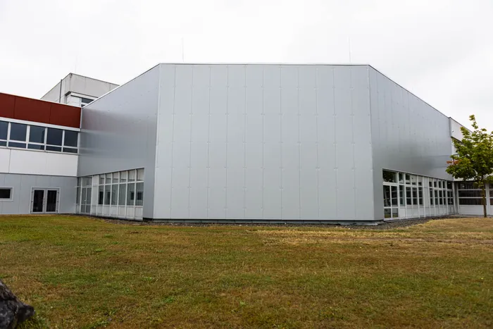 Moderne Fassade der Gesamtschule Kierspe mit hellgrauen Paneelen und großen Fensterfronten im Erdgeschoss.