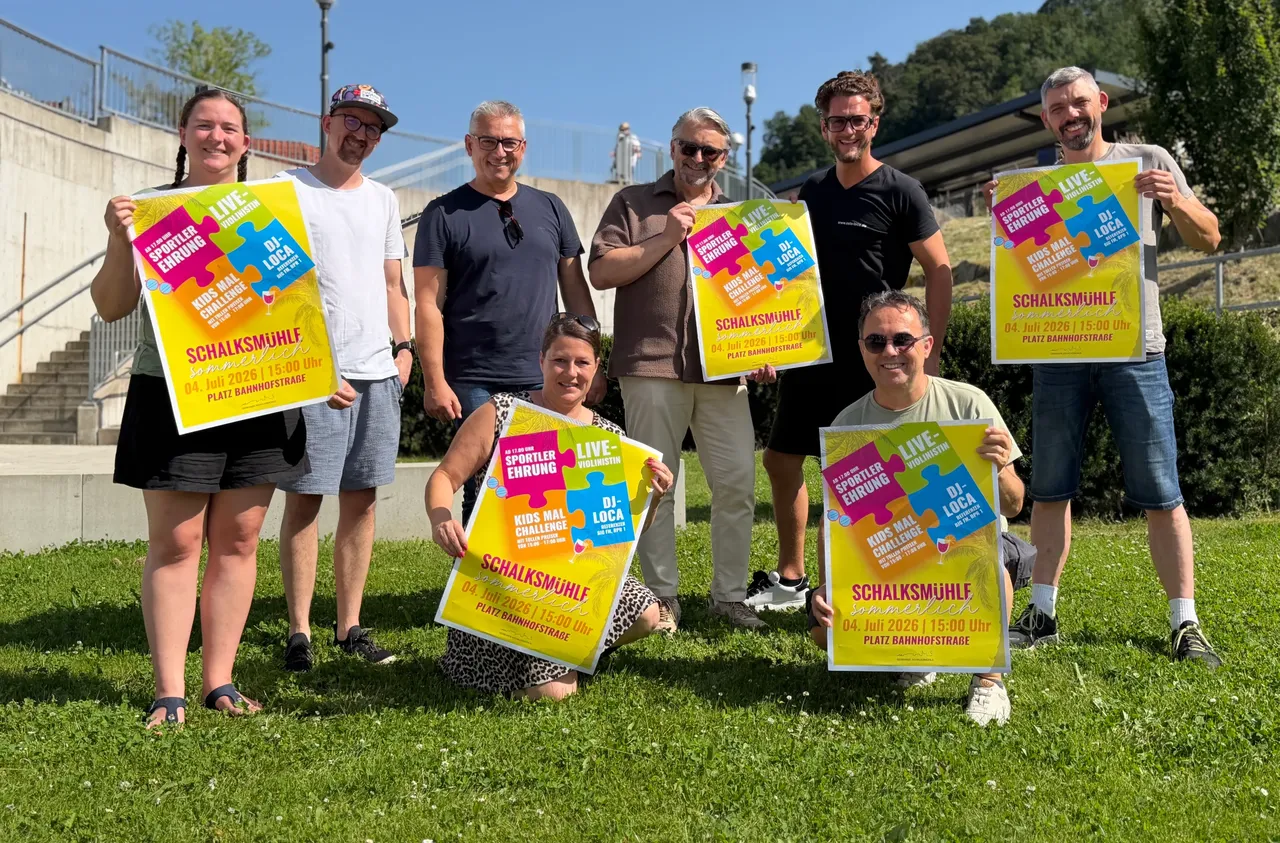 Eine Gruppe von Menschen hält Plakate mit der Aufschrift „Schalksmühle sommerlich“ und „Sportlerehrung“ in der Hand. Im Hintergrund sind Treppen und Gebäude zu sehen.