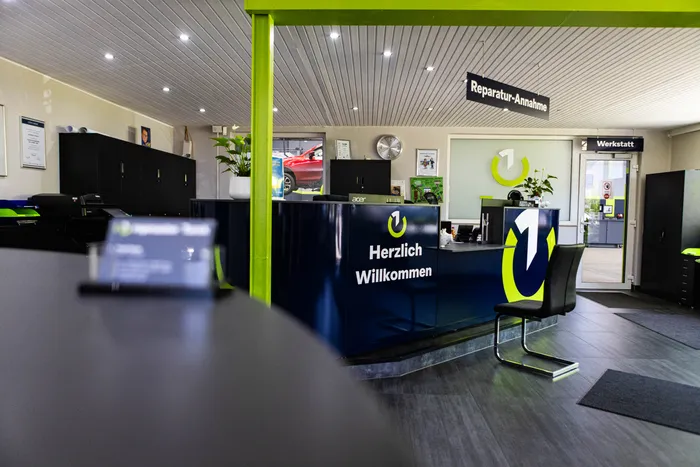 Rezeption einer Autowerkstatt mit dem Schriftzug 'Herzlich Willkommen' und dem Logo der 'repmaster'-Unternehmensgruppe. Im Hintergrund ist ein Schild mit der Aufschrift 'Reparatur-Annahme' zu sehen.