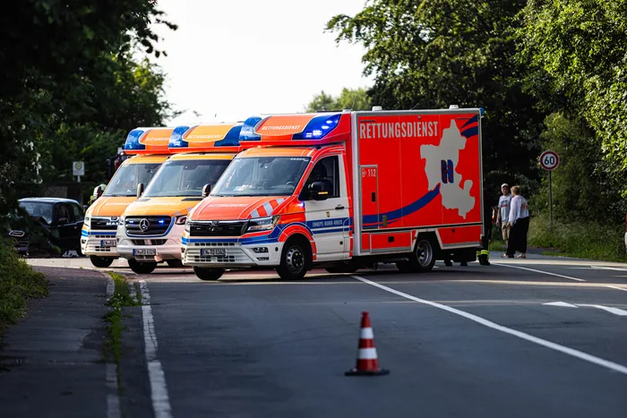 Drei Rettungswagen mit Aufschrift „Rettungsdienst“ stehen an einer Landstraße, neben der ein Auto steht. Ein Verkehrsschild zeigt die Geschwindigkeitsbegrenzung 60.