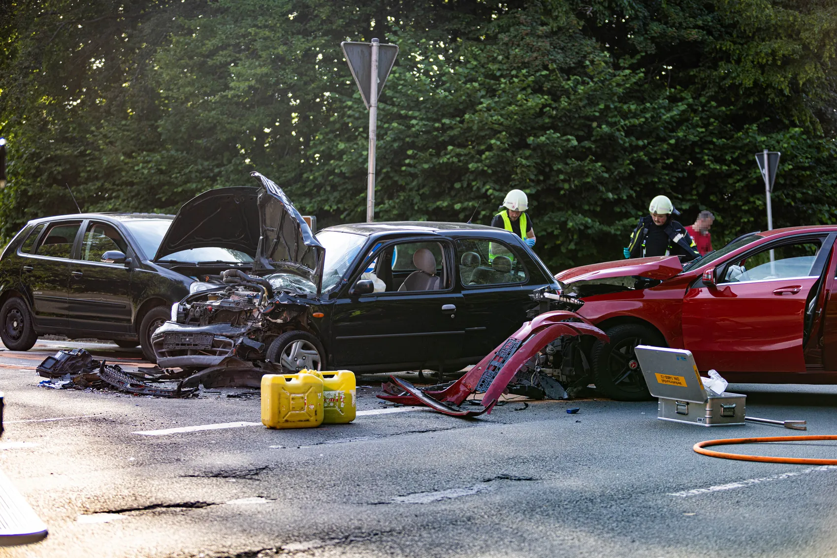 Mehrere stark beschädigte Autos blockieren eine Landstraße nach einem Unfall. Rettungskräfte sind vor Ort und kümmern sich um die Verletzten.