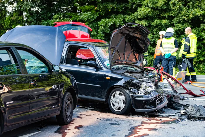 Beschädigte Autos nach einem Unfall auf einer Straße, im Hintergrund Einsatzkräfte der Feuerwehr und des Rettungsdienstes.
