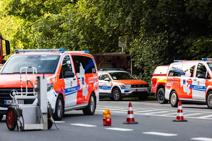 Mehrere Rettungswagen und ein Polizei-SUV sind an einem Unfallort auf einer Straße positioniert. Im Hintergrund sind Bäume und ein Verkehrsschild zu sehen.