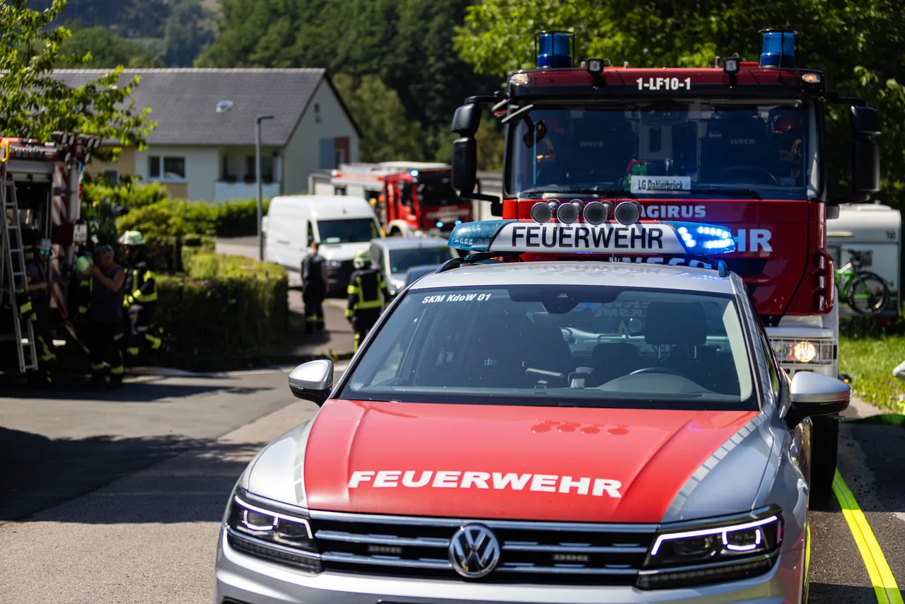 Feuerwehrfahrzeuge, darunter ein roter VW und ein großer roter Löschwagen mit Blaulicht, stehen vor Häusern in Strücken während eines Gasaustritts. Im Hintergrund sind Einsatzkräfte zu sehen.