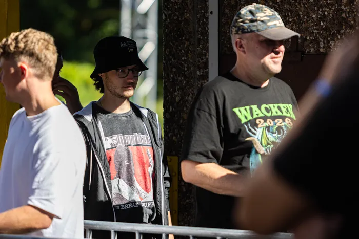 Personen beim Einlass zum Bautz-Freitag Festival, darunter ein Mann mit schwarzem Bucket Hat und ein Mann in einem „WACKEN 2026“ T-Shirt.