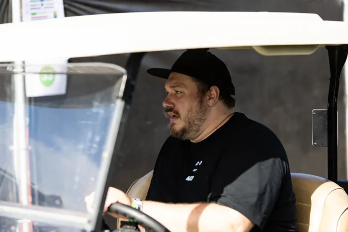 Ein bärtiger Mann mit schwarzer Kappe und schwarzem T-Shirt sitzt am Steuer eines Golfkarrens.