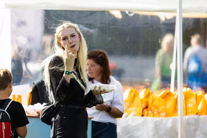 Eine blonde Frau in einem schwarzen Spitzenoberteil hält einen weißen Behälter und macht eine Handbewegung beim Bautz-Festival.