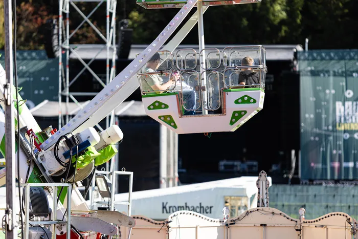 Eine Person sitzt in einer weiß-grünen Gondel eines Fahrgeschäfts vor einer Festivalbühne.