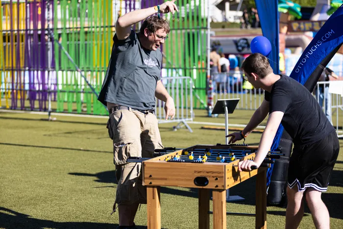 Zwei Männer spielen Tischfußball auf dem sonnigen Bautz-Festival vor einer bunten Kulisse.