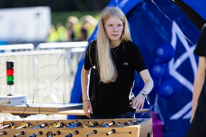 Eine junge Frau mit langen blonden Haaren steht an einem Tischkicker vor einem blauen Zelt auf dem Bautz-Festival.