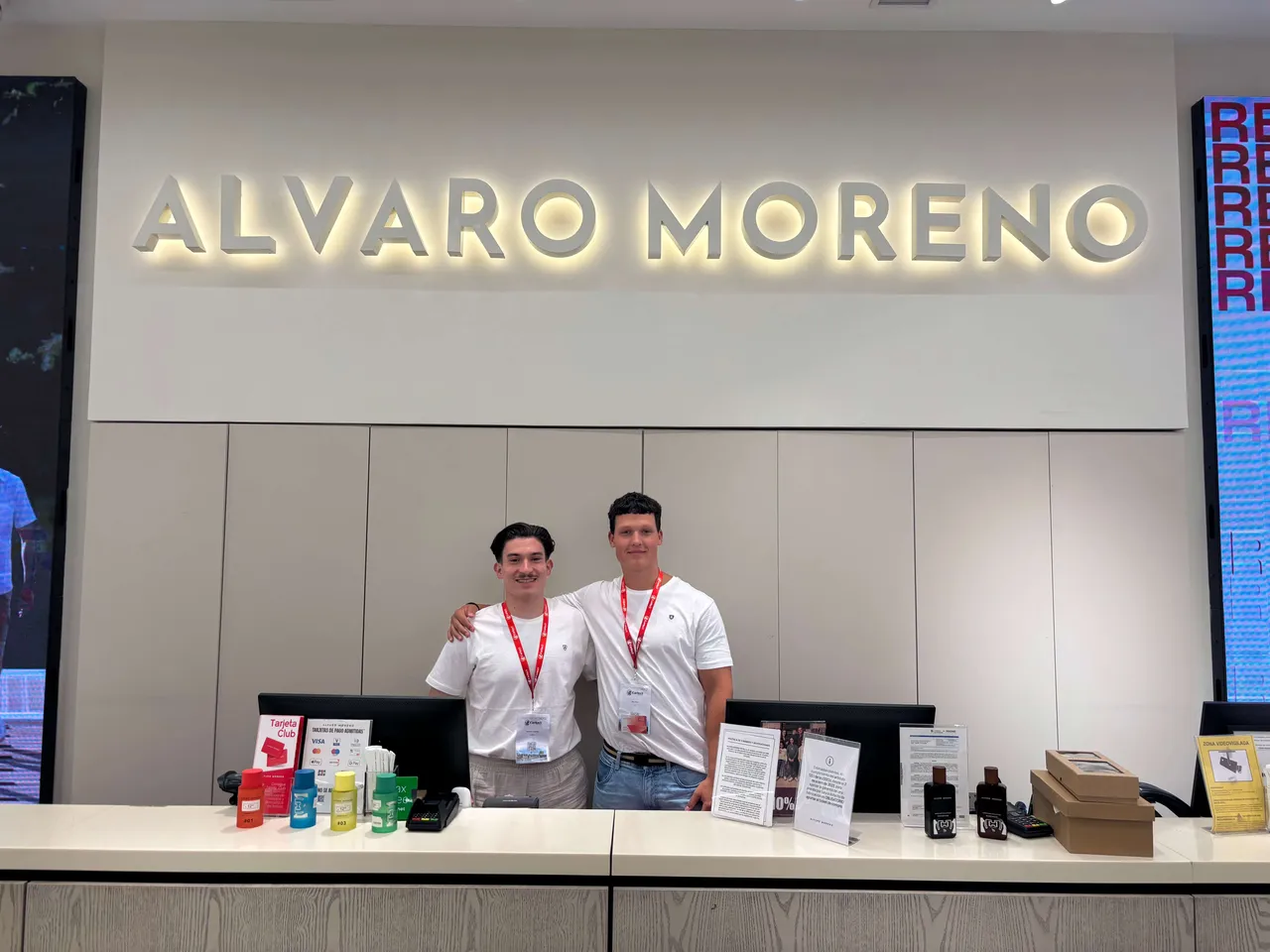 Marc Bober und Giuseppe Trombello stehen hinter einem Verkaufstresen vor einem beleuchteten „ALVARO MORENO“-Schriftzug.