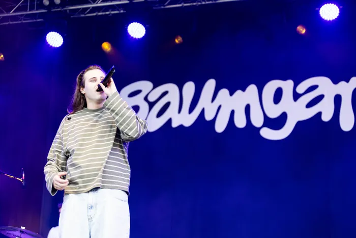 Baumgart singt mit einem Mikrofon auf der Bühne des Bautz-Festivals vor einem blau beleuchteten Hintergrund mit weißem Schriftzug.
