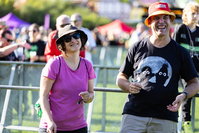 Eine lächelnde Frau in einem rosa T-Shirt und Baumgart mit orangefarbenem Hut stehen vor einem Metallzaun auf dem Bautz-Festival.