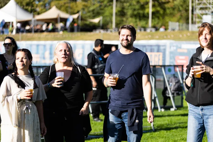 Menschen mit Getränken in Plastikbechern gehen über das Gelände des Bautz-Festivals 2026 vor Zelten und Bühnenstrukturen.