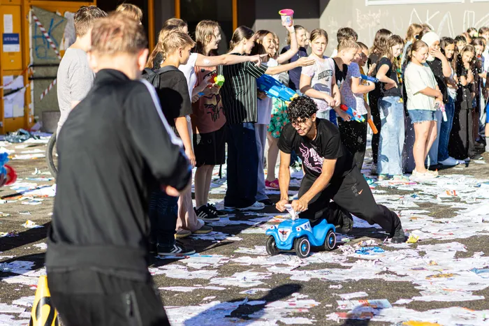 Schüler feiern eine Wasserschlacht auf dem Schulhof der Rothensteinschule, umgeben von Konfetti. Ein Schüler kniet und bedient ein ferngesteuertes Auto.