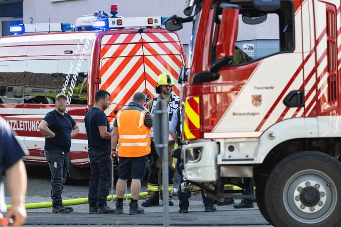 Feuerwehrleute besprechen die Situation vor einem roten Feuerwehrauto und einem weißen Einsatzwagen nach Beschädigung einer Gasleitung bei Bauarbeiten in Meinerzhagen.