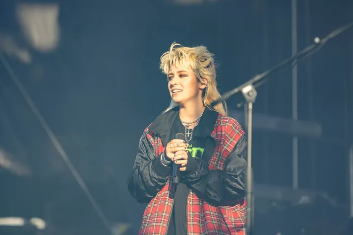 Paula Carolina singt mit einem Mikrofon auf der Bühne des Bautz-Festivals in einer rot-schwarz karierten Jacke.