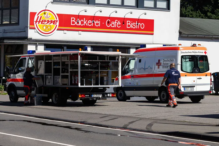Rettungswagen und Begleitfahrzeug des Deutschen Roten Kreuzes vor einem Gebäude, im Hintergrund eine Bäckerei. Im Zusammenhang mit Bauarbeiten wurde eine Gasleitung beschädigt.