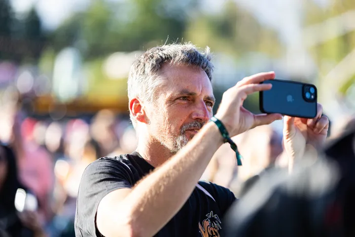 Ein Mann mit grauem Haar und Bart hält ein Smartphone hoch, um ein Foto oder Video zu machen.