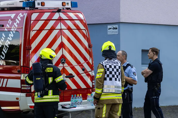 Feuerwehrleute und Polizisten besprechen die Situation vor einem roten Einsatzwagen nach einer Beschädigung einer Gasleitung bei Bauarbeiten.