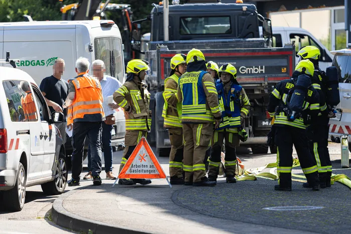 Feuerwehrleute sind bei Bauarbeiten in Meinerzhagen nach Beschädigung einer Gasleitung im Einsatz. Ein Warnschild weist auf Arbeiten an Gasleitungen hin.