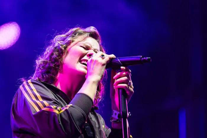 Sängerin der Band Juli singt mit geschlossenen Augen in ein Mikrofon unter violettem Bühnenlicht.