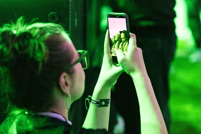 Eine Person mit einem Crew-Armband fotografiert die Band Juli mit einem Smartphone unter grünem Licht.