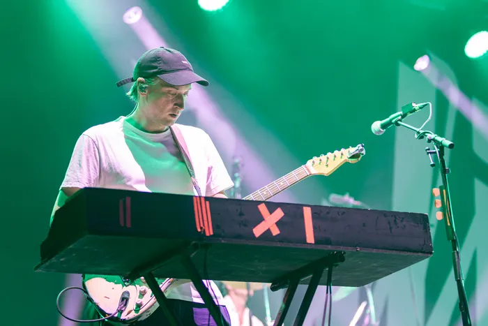 Ein Musiker der Band Juli mit schwarzer Kappe spielt unter grünem Bühnenlicht an einem Keyboard.
