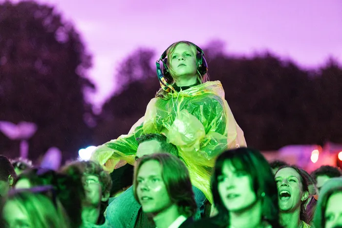 Eine Person mit Kopfhörern und gelbem Regenmantel blickt in einer Menschenmenge bei einem Musikfestival nach oben.