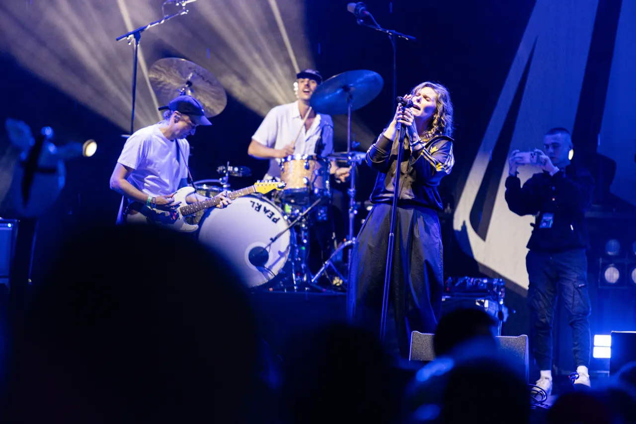 Die Band Juli tritt bei blauem Bühnenlicht live auf, mit der Sängerin im Vordergrund und einem Gitarristen sowie Schlagzeuger im Hintergrund.
