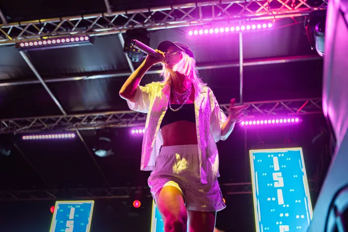 Isi Glück singt mit einem Mikrofon auf einer Bühne unter pinkfarbenem Licht.