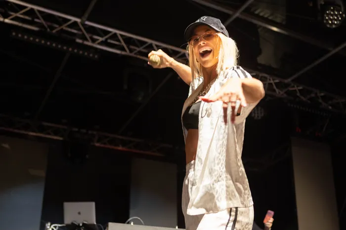 Isi Glück singt mit einem Mikrofon auf der Bühne beim Bautz Festival 2026. Sie trägt eine schwarze Kappe, eine Brille und ein weiß gemustertes Outfit.