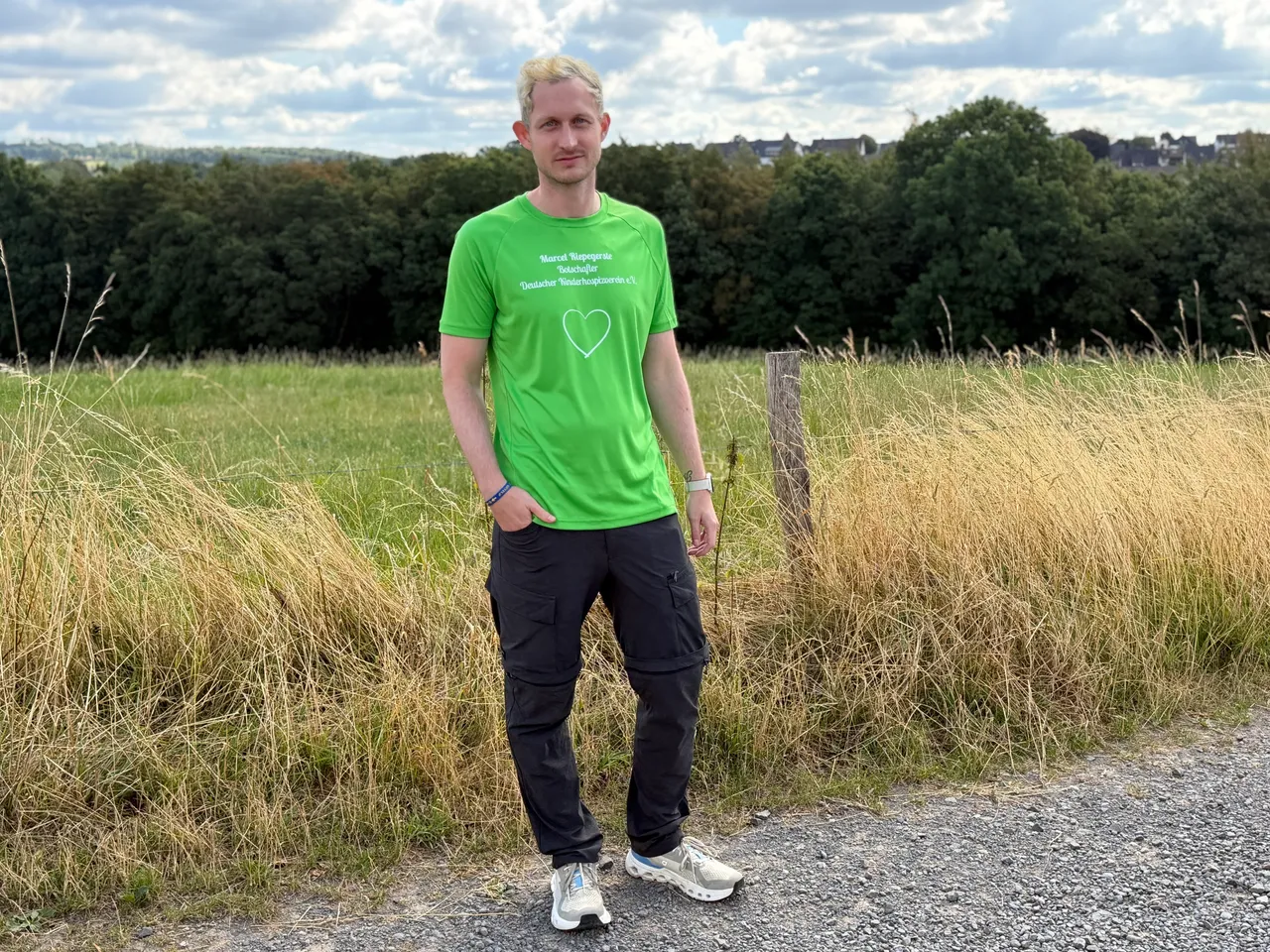 Marcel Riepegerste steht in einem Feld mit hohem Gras und trägt ein grünes T-Shirt mit einem weißen Herz.