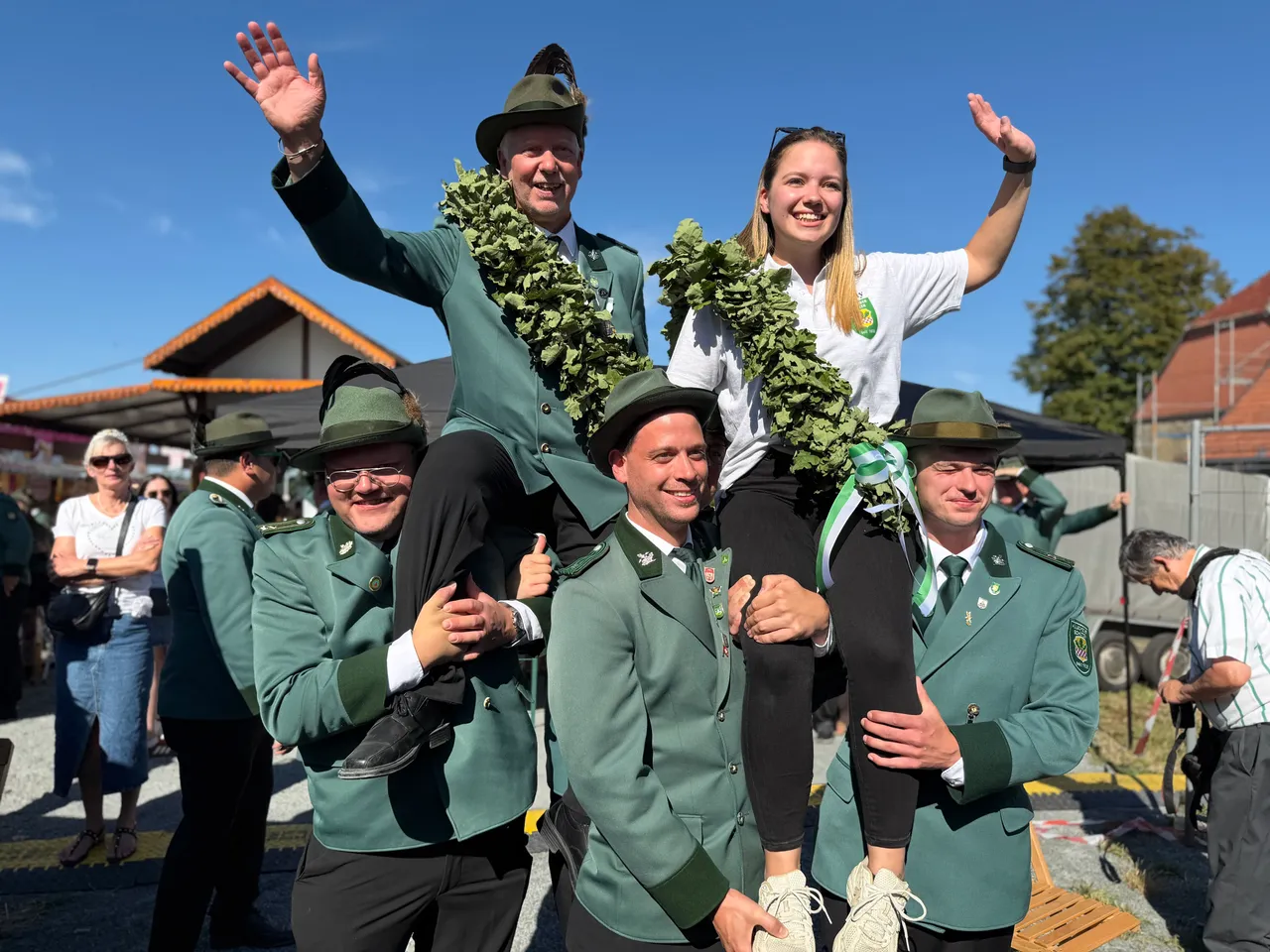 Schützenkönig Uwe Bahr und Jungschützenkönigin Emily Keizer werden auf den Schultern von Männern in grünen Uniformen getragen und tragen grüne Kränze.