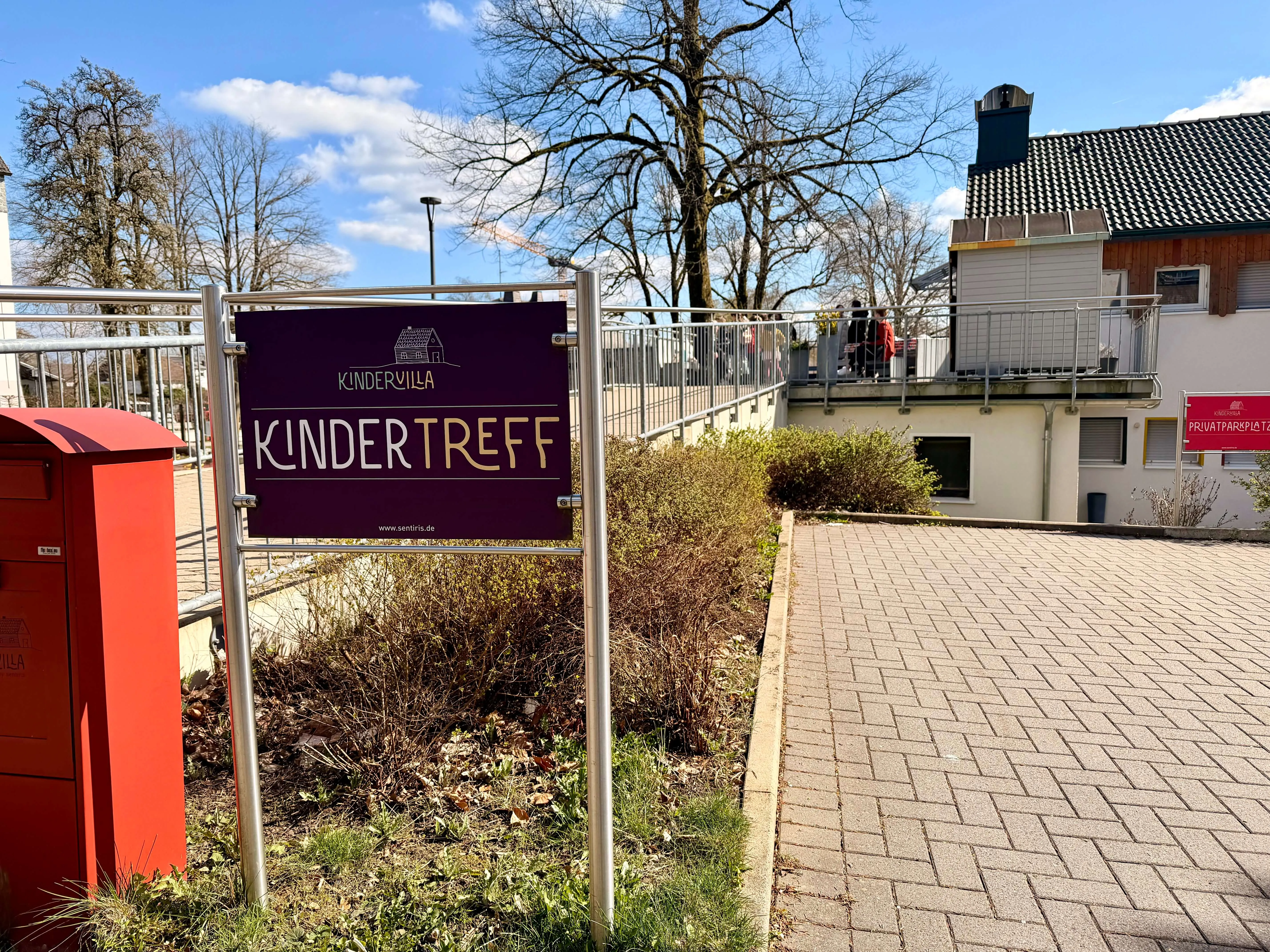 Schild „Kindervilla Kindertreff“ vor einem Gebäude mit einem roten Briefkasten davor.