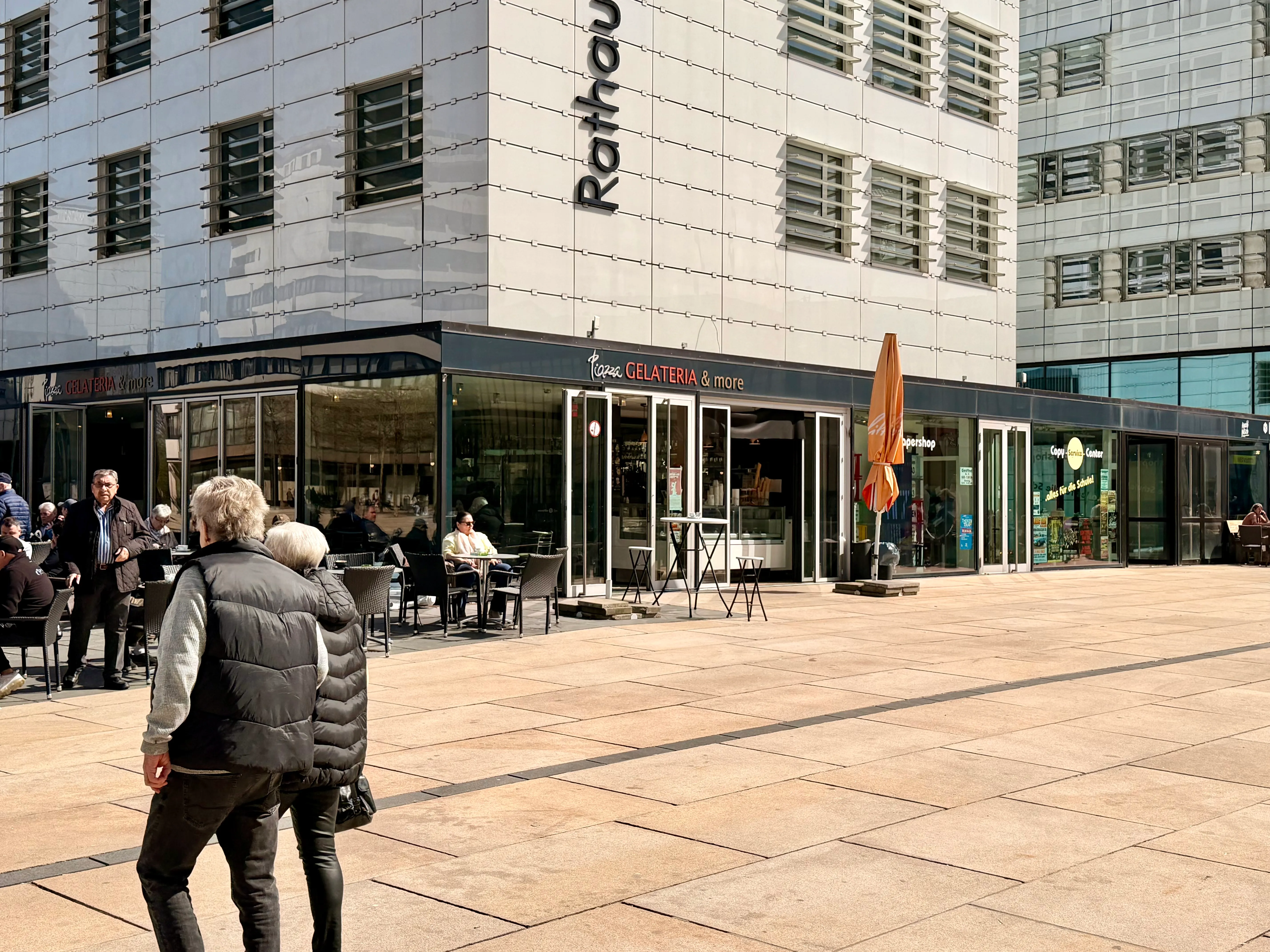Das Eiscafé „Zentro“ mit Außenbereich befindet sich vor einem modernen Glasgebäude mit dem Schriftzug „Rathaus“.
