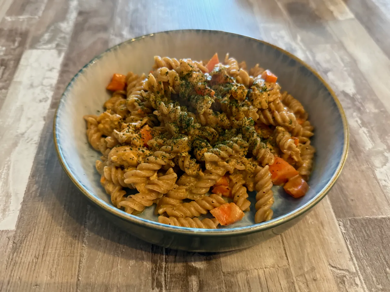 Eine Schüssel mit Fusilli-Nudeln und gewürfelten Möhren in cremiger Soße, bestreut mit Kräutern.