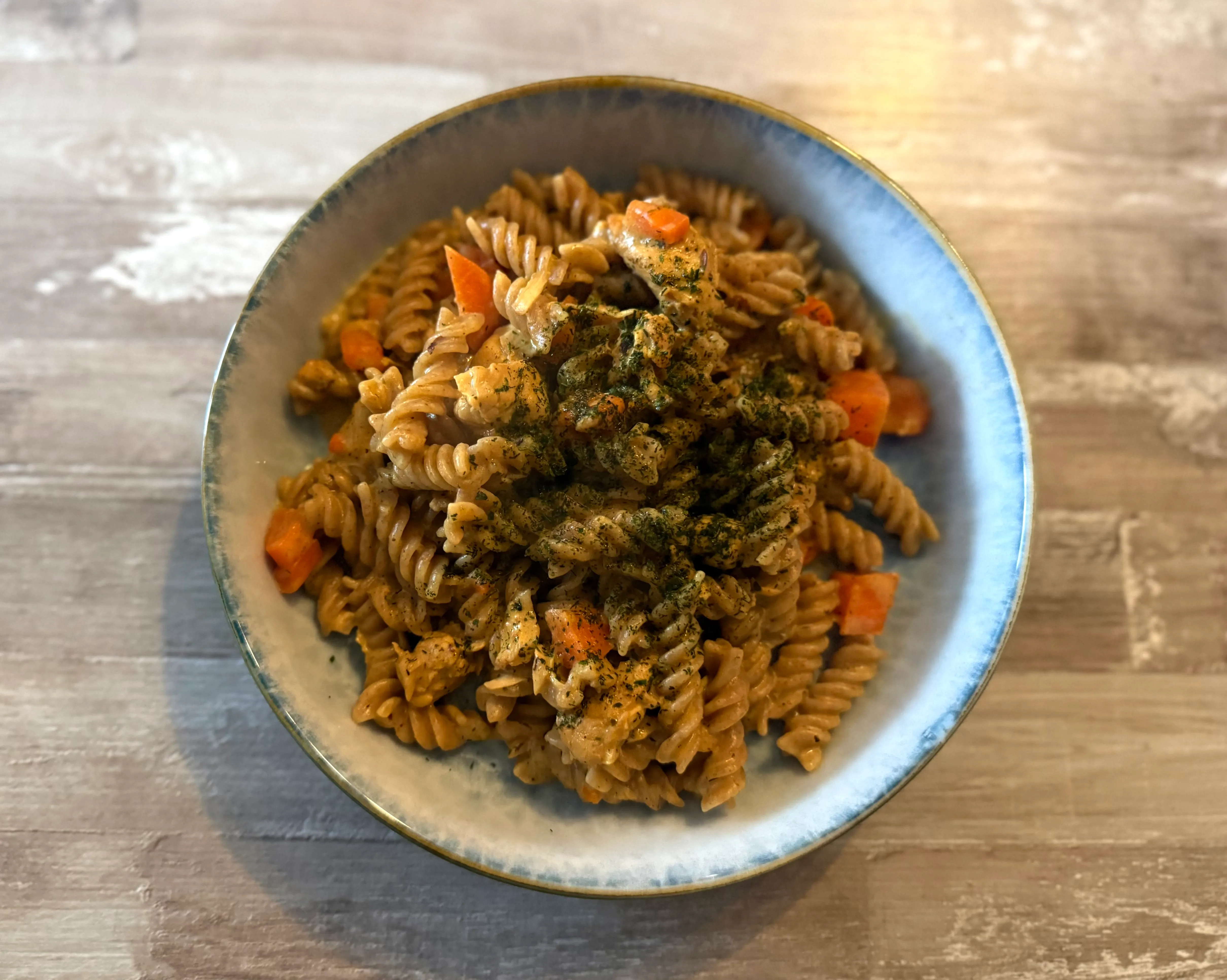 Eine Schüssel mit Fusilli, Karottenstücken und einer cremigen Soße mit Kräutern.